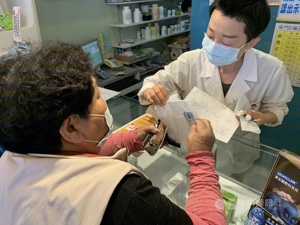 A pharmacist (right) hands a woman two masks after swiping her National Health Insurance (NHI) card, one of the many ways the NHI card has been used in COVID-19 measures.