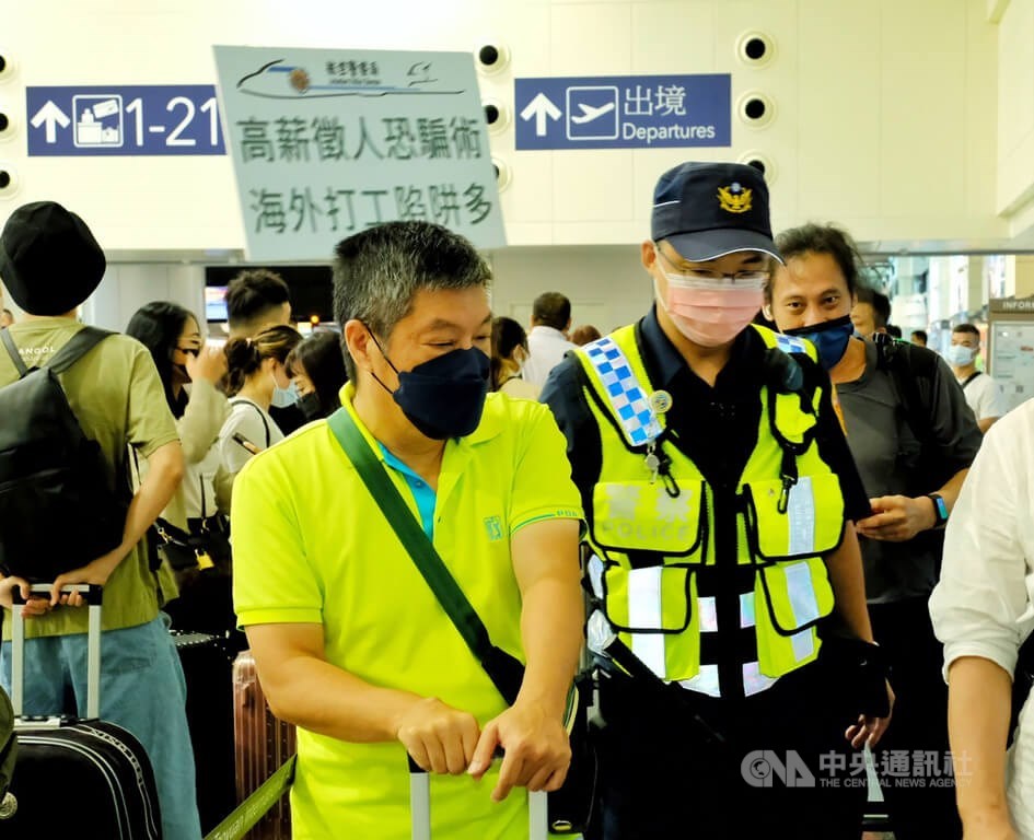 A policeman chats with passengers planning to travel to Cambodia with a sign warning risks of job scams at Taiwan Taoyuan International Airport on Monday. CNA photo Aug. 15, 2022
