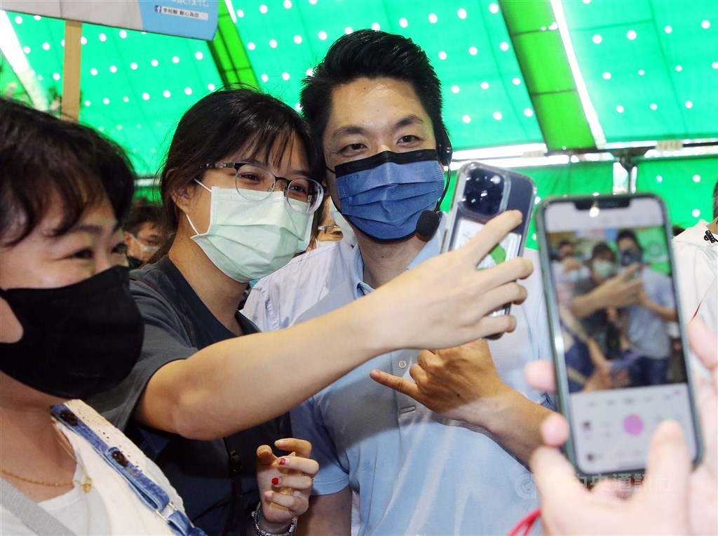 Kuomintang (KMT) Taipei mayoral candidate Chiang Wan-an (蔣萬安) takes a selfie with a passerby at the Jianguo Holiday Flower Market while on the campaign trail on Sunday. CNA photo Nov. 20, 2022
