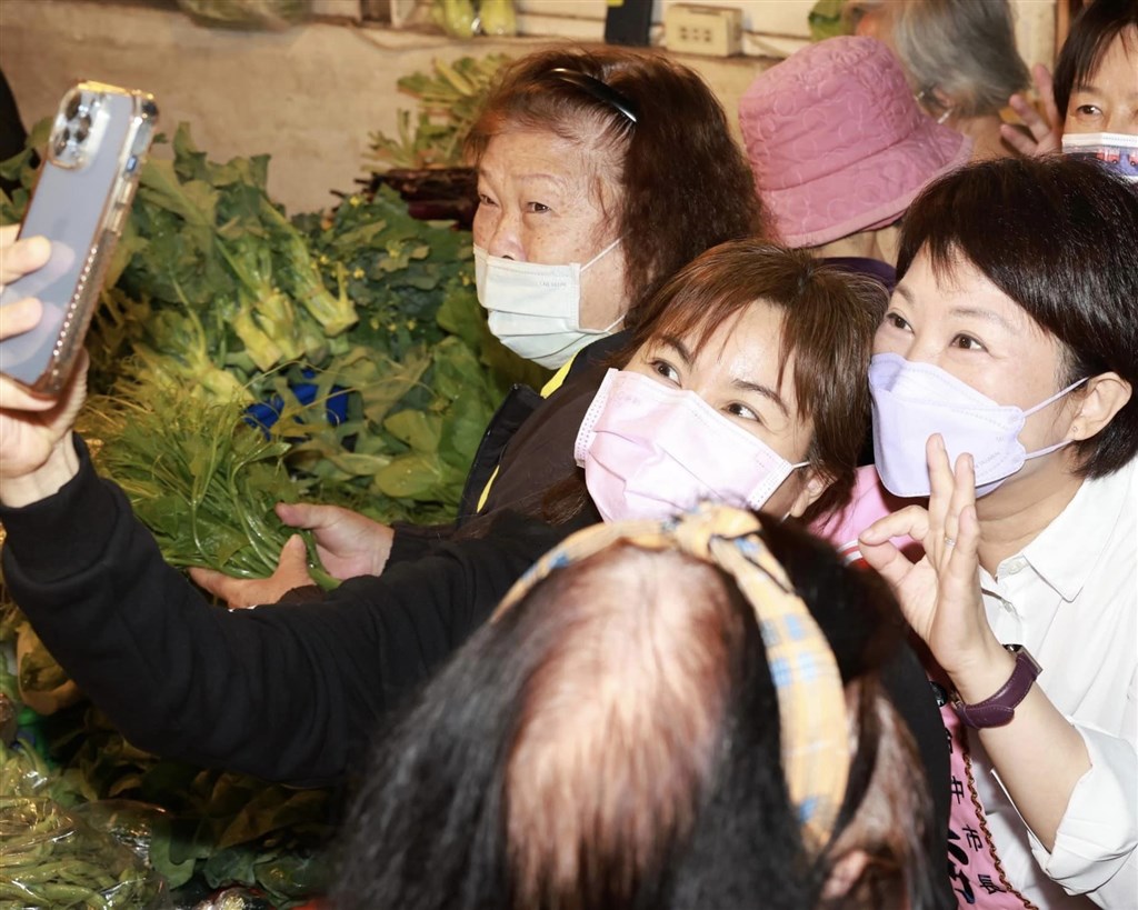 Taichung Mayor Lu Shiow-yen (盧秀燕, right) of the opposition KMT raises three fingers -- her number on the election ballot -- when taking a picture with supporters in a local market as she campaigns for a second term on Tuesday. Photo taken from Lu Shiow-yen