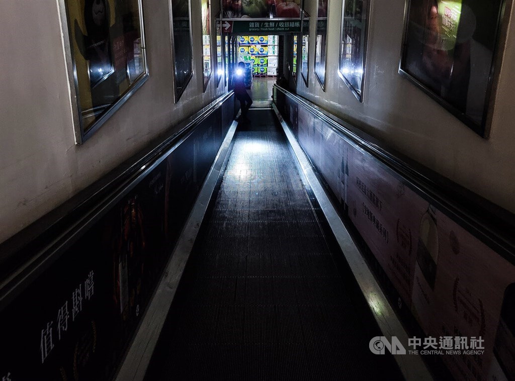 A hypermarket worker uses a flashlight to guide shoppers on a stalled inclined moving walkway in Taipei on March 3, when 5.49 million households and businesses were hit by a nationwide power outage caused by a malfunction at Kaohsiung