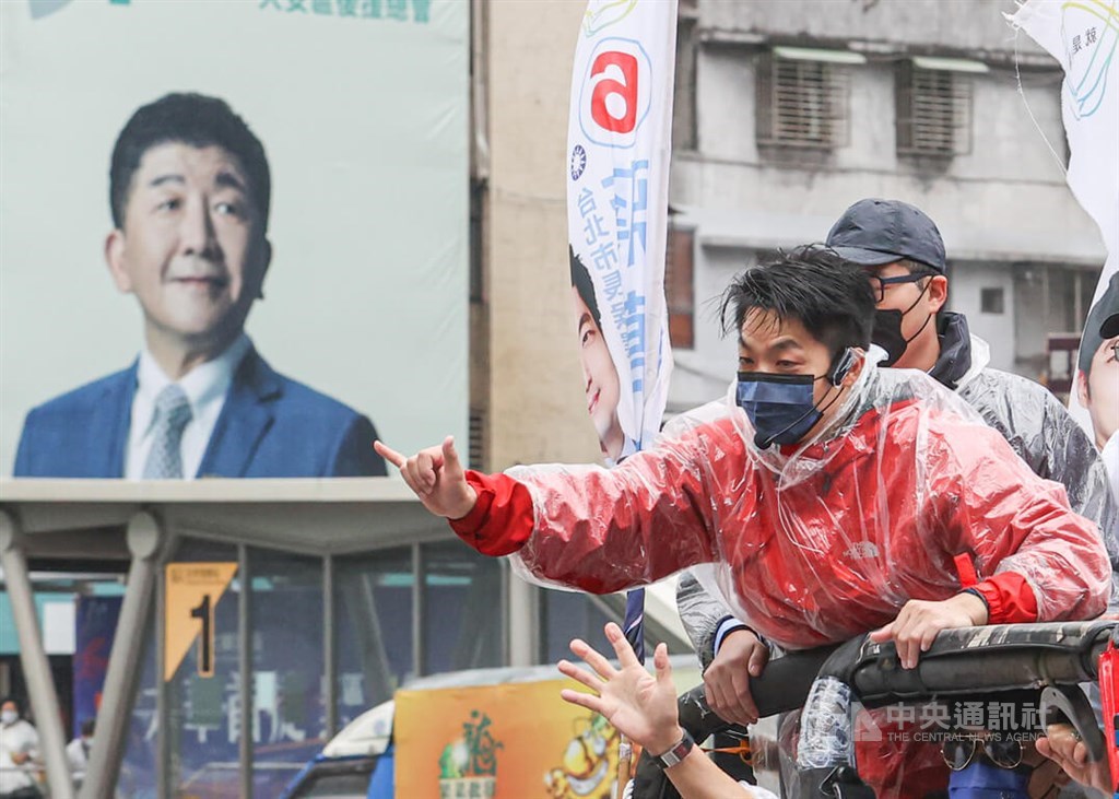 Chiang Wan-an (蔣萬安, front), the opposition Kuomintang candidate for Taipei mayor, passes by a billboard showing one of his opponents, former Health Minister Chen Shih-chung (陳時中, left), as he campaigns in Taipei on Nov. 24. Chiang took office on Dec. 25 after winning the Nov. 26 election.