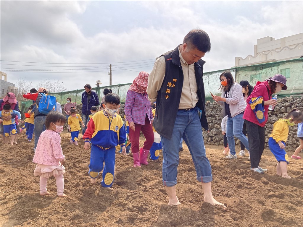 Penghu Huxi Township chief Chen Chen-chung (陳振中, front) kicks the earth with kids to plant peanuts in an activity held by the township office Friday. Photo: Penghu Huxi Township Office