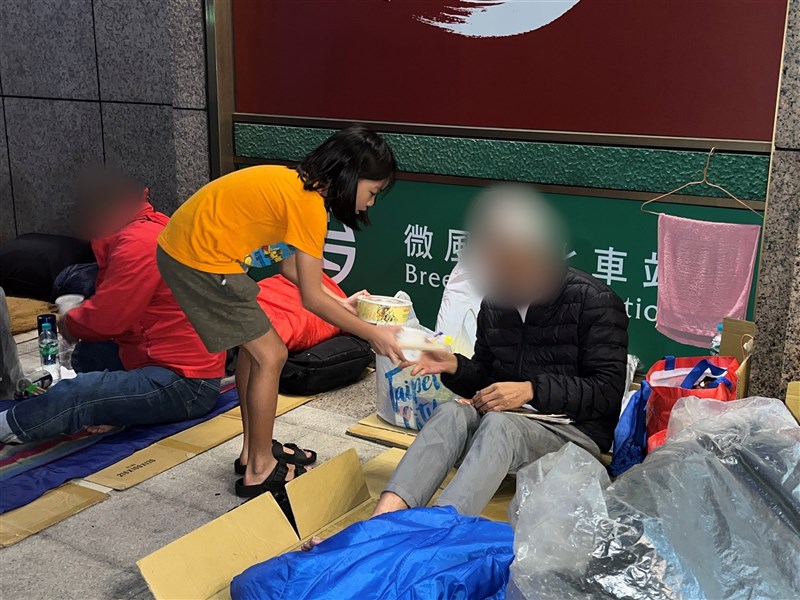 Shu-you (書偊), 9, gets involved by handing a warm meal to a homeless individual outside Taipei Main Station during the year-end banquet. CNA photo Jan. 22, 2024