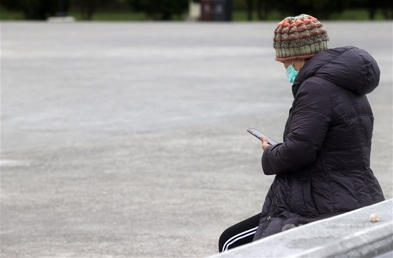 A women in warm clothes sits and checks her phone in Taipei Sunday. CNA photo Feb. 25, 2024
