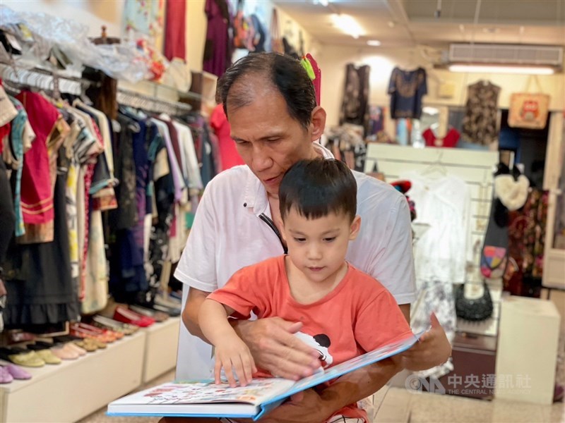 Lin reads a picture book with his son An, who was born through a surrogate mother, at his souvenir shop in New Taipei. CNA photo June 15, 2024