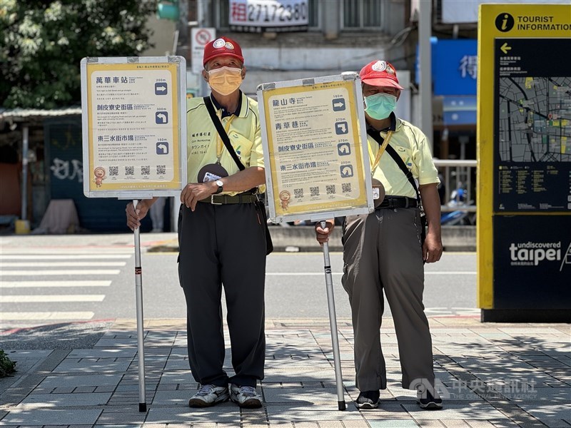 City Navigator Tung (left) and his colleague hold signs with directions to nearby attractions outside Longshan Temple Station in Taipei on a Thursday morning. CNA photo Aug. 31, 2024