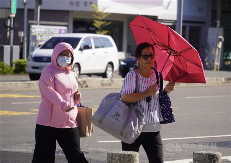 Pedestrians in Kaohsiung cross a street while shielding themselves from the sun with a jacket and umbrella (CNA file photo).