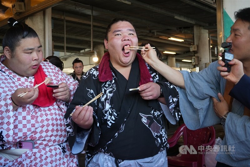Sumo wrestlers in traditional Japanese garb enjoy raw fish slices at a seafood market by Donggang Fishery Port in Pingtung County Monday. CNA photo June 9, 2025