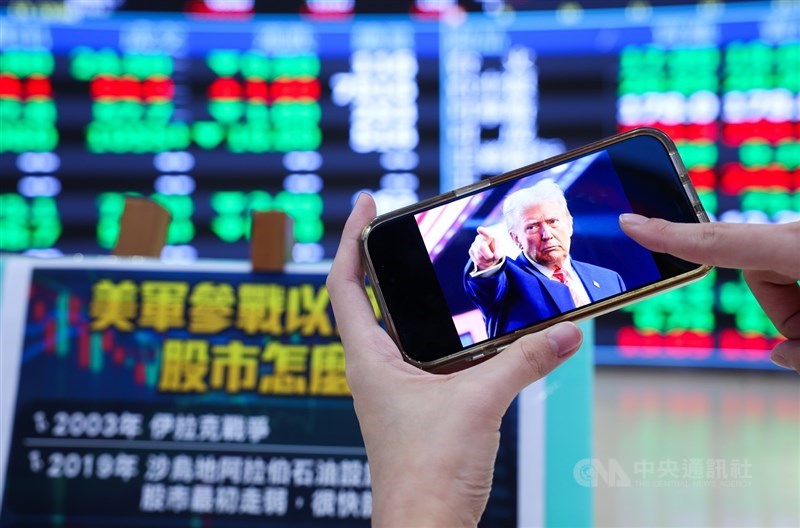 A person holds a smartphone displaying a photo of U.S. President Donald Trump in front of an electronic stock board in Taipei on Monday. CNA photo June 23, 2025
