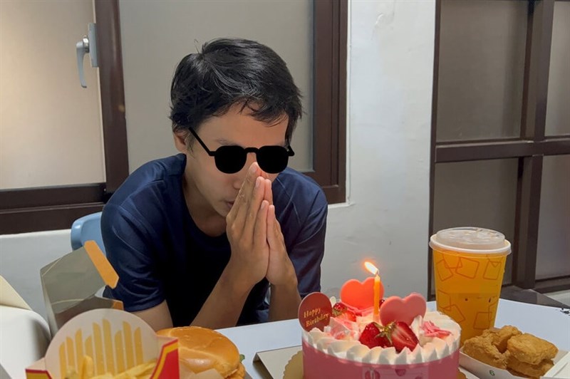 A young man (digitally masked for privacy) makes a wish in front of a lit cake, surrounded by fast food items. Photo courtesy of the Taichung Social Affairs Bureau