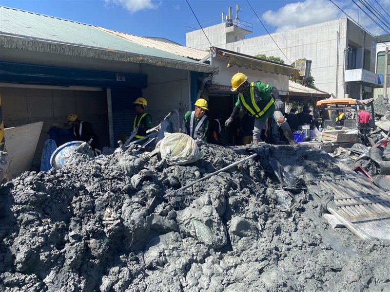 Migrant workers work to remove a thick layer of mud from a street in Guangfu Township, Hualien County Sunday. Photo courtesy of Welldoer House