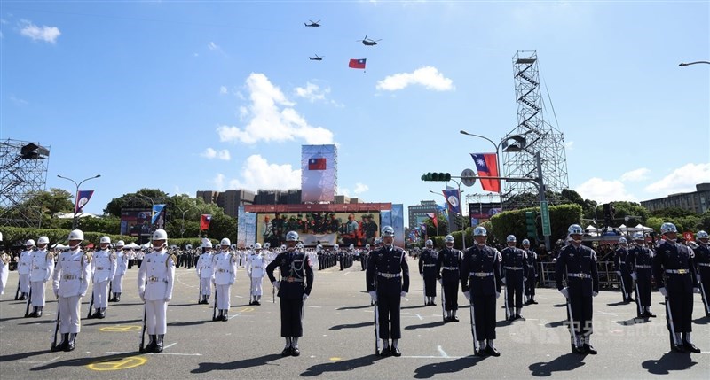 Honor Guards stand in attention while a CH-47SD Chinook flies the nation's flag across the sky, chaperoned by two UH-60M Black Hawk helicopters. CNA photo Oct. 10, 2025