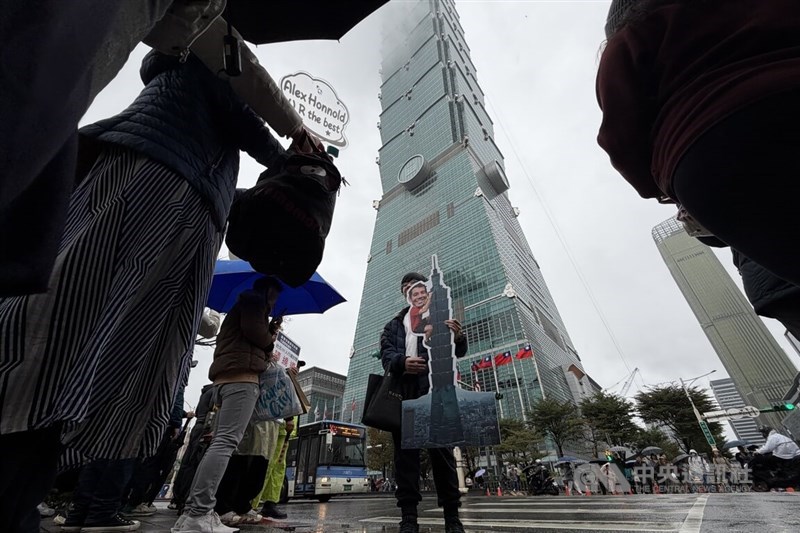 A man holds a cardboard cutout supporting climber Alex Honnold in front of Taipei 101 on Saturday. CNA photo Jan. 24, 2026