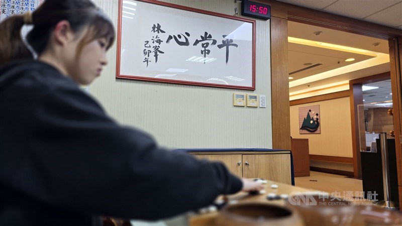 Yang Tzu-hsuan places stones against a calligraphic work by Taiwanese Go legend Lin Hai-fong (林海峰), who is based in Japan, bearing the word “composure,” at the HaiFong Go Academy in Taipei on Feb. 10. CNA photo, Feb. 16, 2026