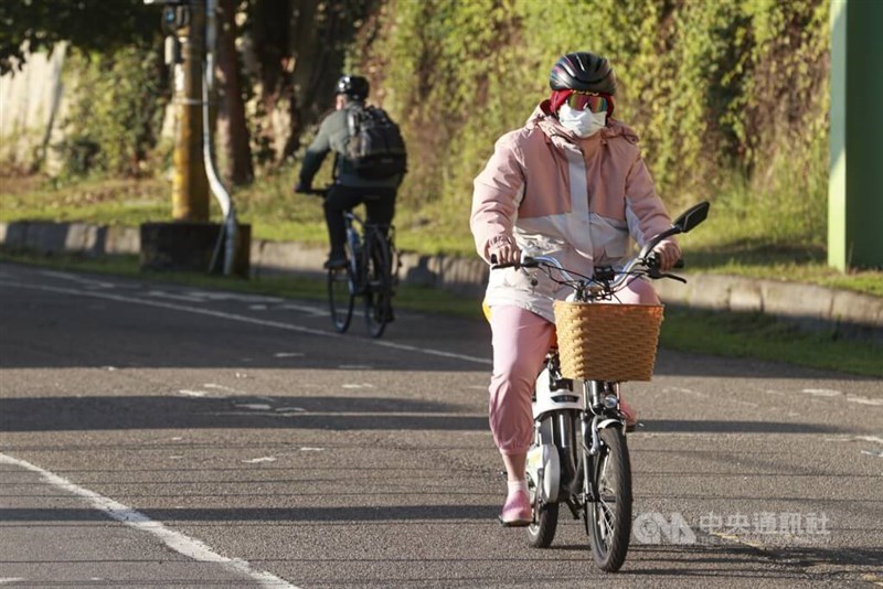 A woman in warm clothing rides a bicycle along a riverside path in Taipei. CNA file photo