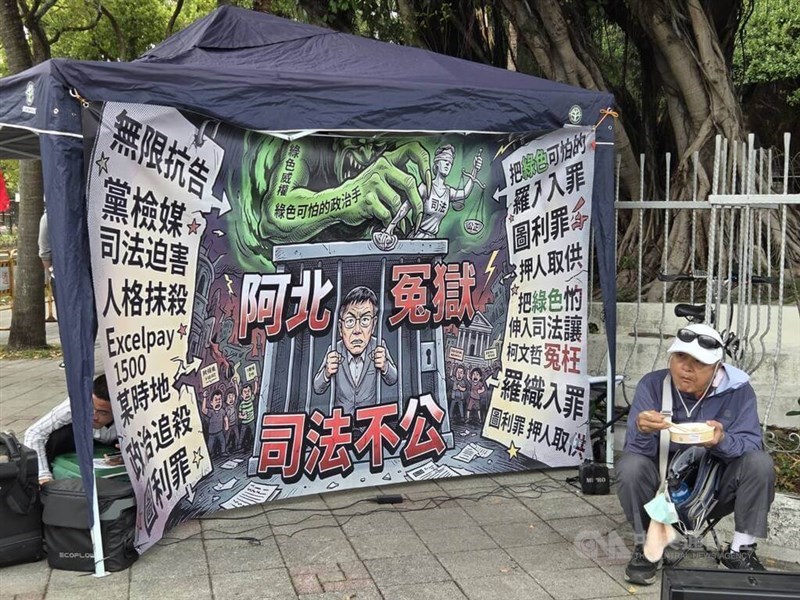 A large banner depicting former Taipei Mayor Ko Wen-je detained by a “green devil” with slogans reading “wrongful imprisonment” and “judicial injustice” is displayed by a supporter of Ko outside the Taipei District Court ahead of Ko’s verdict on Thursday. CNA photo March 27, 2026