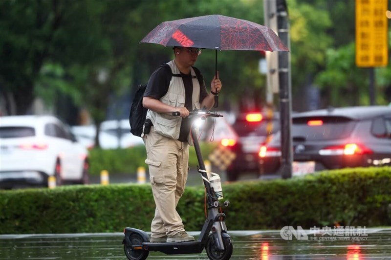 A man rides an e-scooter while holding an umbrella in Taoyuan. CNA file photo