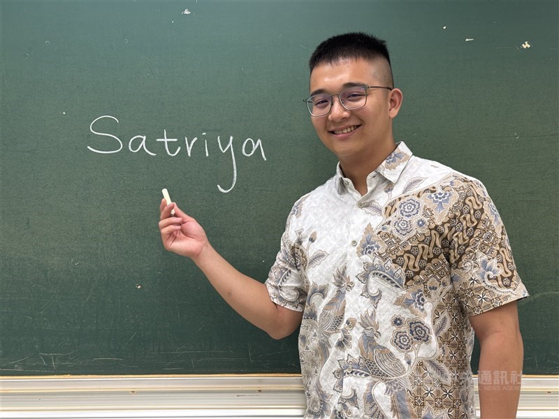 National Chengchi University (NCCU) student Ethan Huang poses beside his Indonesian name, “Satriya,” written on a classroom blackboard at the school in Taipei in late May. CNA photo Aug. 12, 2026