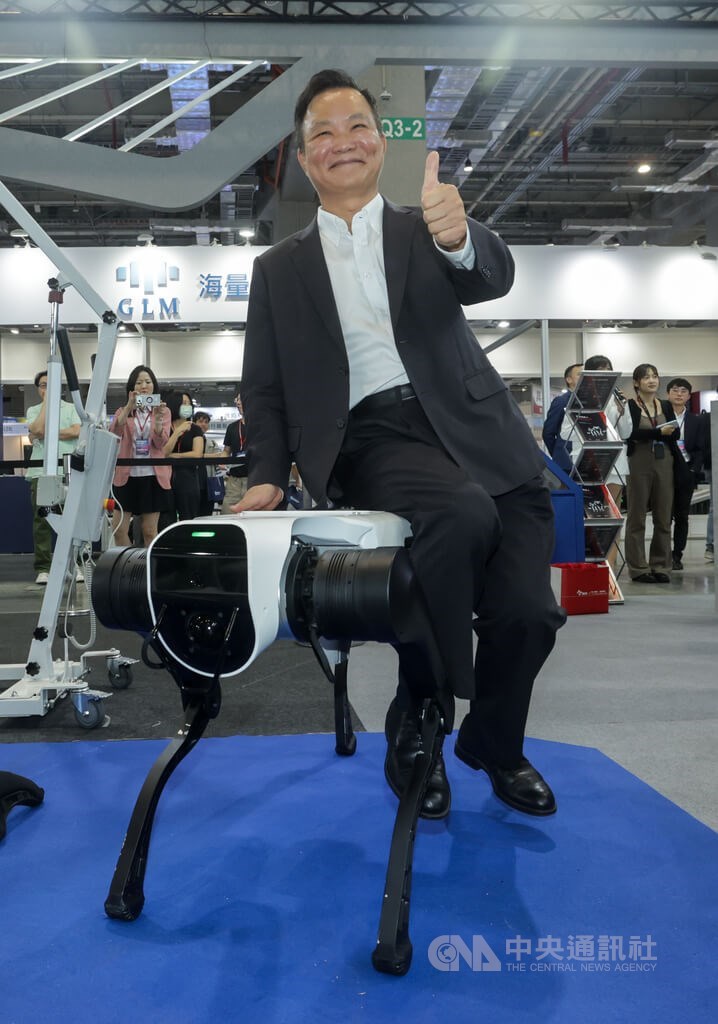 Swancor Robotech Co. Chairman Jauyang Tsai (front) gives a thumbs-up while sitting on a robot dog at Automation Taipei at Nangang Exhibition Hall in Taipei on Wednesday. CNA photo Aug. 19, 2026