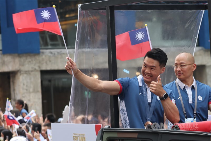 Peraih medali perunggu palang tunggal putra Tang Chia-hung (kiri) dan pelatihnya Wen Shih-hang melambaikan bendera dan bersorak selama parade pada hari Jumat. (Sumber Foto : CNA, 16 Agustus 2024)