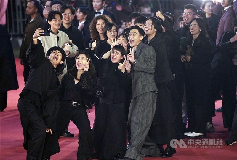 Pembawa acara Liu Kuan-ting (tengah, dalam setelan abu-abu) memberikan tanda kemenangan bersama para peserta acara di karpet merah.(Sumber Foto : CNA, 23 November 2024)