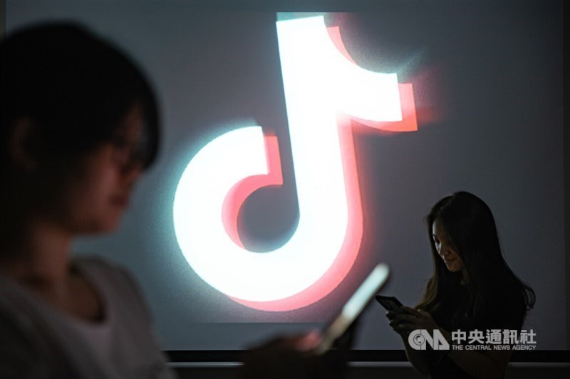 Dua orang menggunakan smartphone mereka di depan logo TikTok yang sangat besar. (Sumber Foto : Dokumentasi CNA)