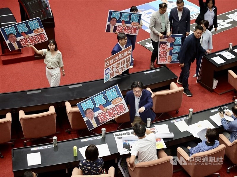 Legislator Partai Progresif Demokratik memegang poster yang menyerukan agar Huang (memakai kaos putih) dirujuk ke Komite Disiplin Yuan Legislatif. (Sumber Foto : CNA, 20 Juni 2025)