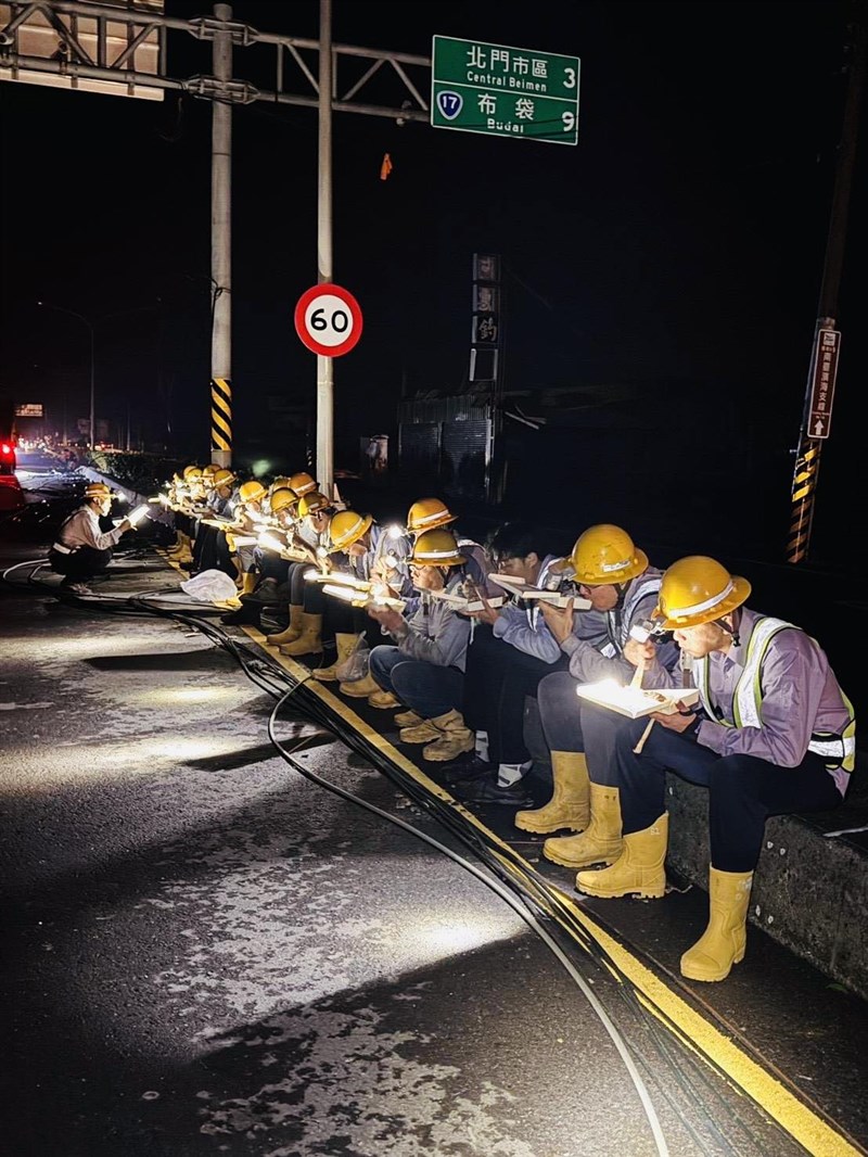 Petugas Taiwan Power Co. makan dan menyeruput air sejenak di pinggir jalanan Tainan pada pukul 8 malam hari Senin sebelum melanjutkan perbaikan. (Sumber Foto : Facebook Taiwan Power Co., 7 Juli 2025)