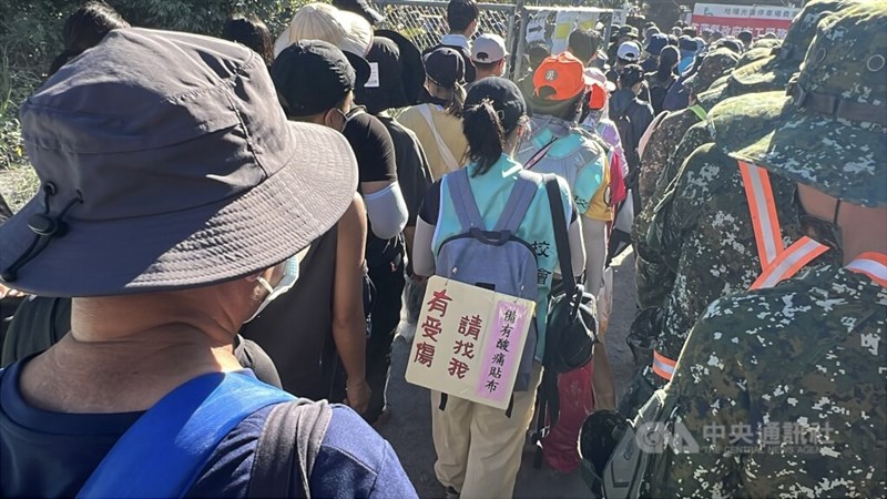 Seorang wanita membawa papan bertuliskan, "Jika Anda terluka, datanglah kepada saya -- saya punya plester pereda nyeri," berdiri di peron Stasiun Guangfu di Kabupaten Hualien bersama para tentara dan relawan lainnya pada hari Sabtu. Foto CNA 4 Oktober 2025