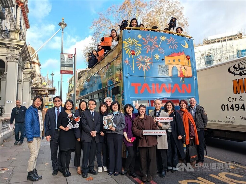 Ilustrator asal Inggris, Hannah Gibson (kelima dari kanan di bawah), dan pejabat pariwisata Taiwan berpose untuk foto bersama sebuah bus wisata yang dilapisi ilustrasi bertema Taiwan karya Gibson di London, Inggris. (Sumber Foto : CNA, 13 Desember 2025)