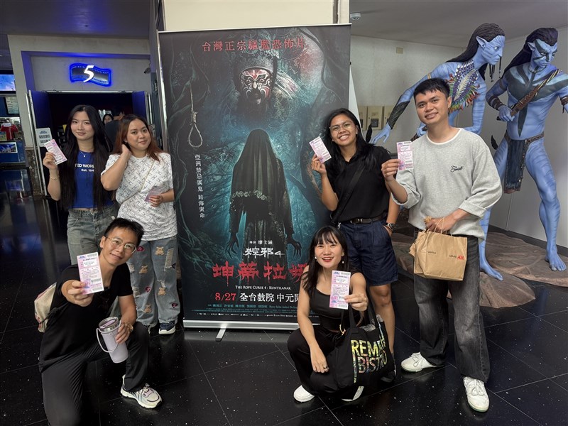 Para diaspora Indonesia yang berfoto menunjukkan tiketnya di depan poster The Rope Curse 4: Kuntilanak sebelum film dimulai. (Sumber Foto : CNA, 23 Agustus 2026).