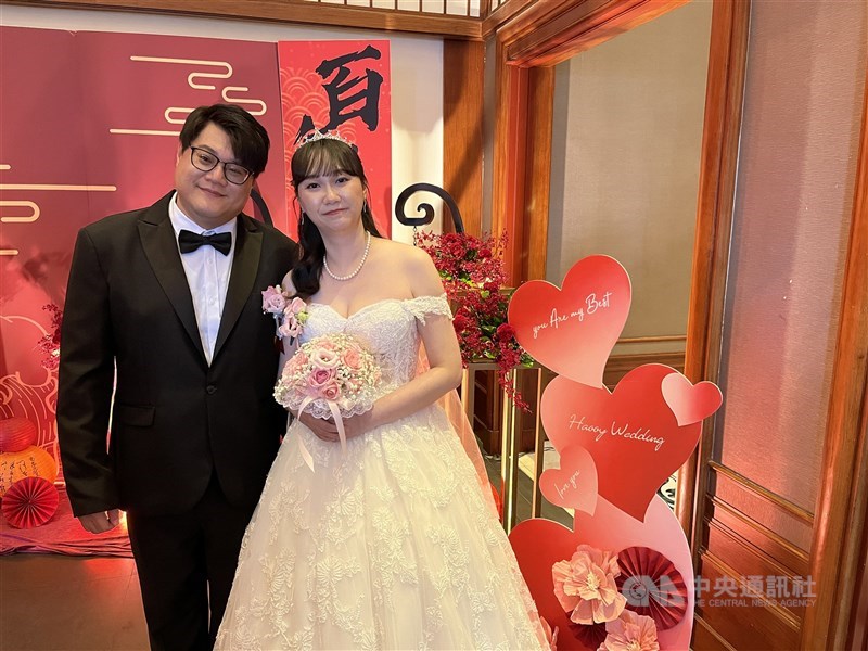 Lin Kuan-nan (kiri) dan istrinya, Grace Huang, berpose di depan dekorasi pernikahan pada sebuah pernikahan massal di Taipei pada Minggu. (Sumber Foto : CNA, 13 September 2026)