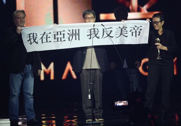 「私はアジアにいる アメリカ帝国反対」と書かれた横断幕を無言で掲げたブラックリスト・スタジオのメンバー