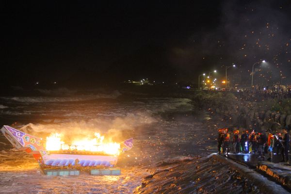 人々に見守られながら、炎を上げて海の中に流される1基目の水灯。