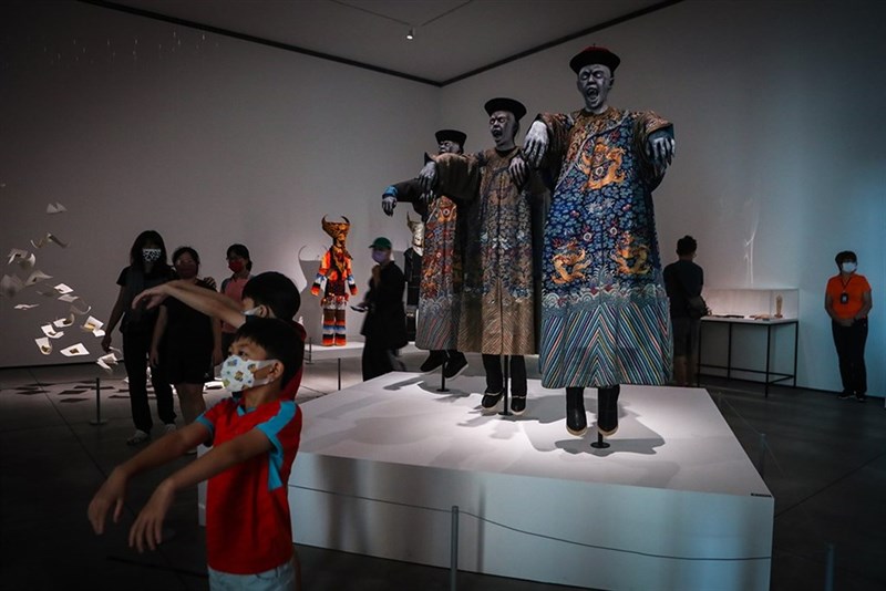 「アジアの幽霊と地獄」展で展示された3体のキョンシーと同じポーズで記念撮影する子供（撮影：王騰毅）