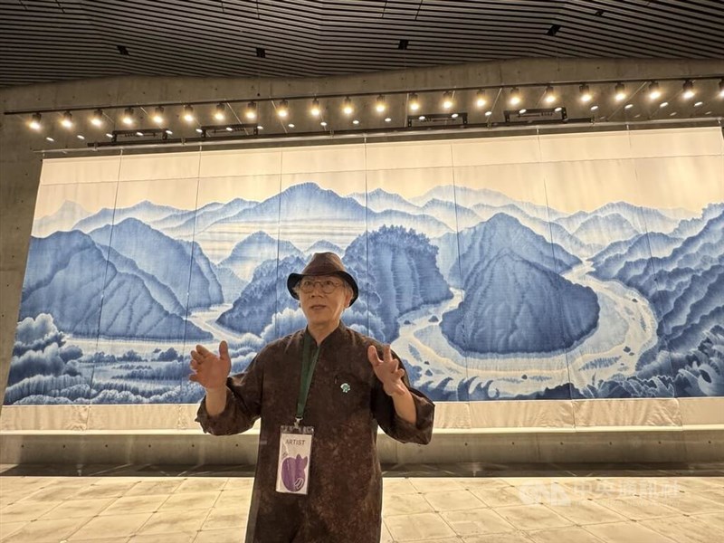 芸術家の陳景林さん。背景は陳さんが手掛けた幅9メートル20センチ、高さ2メートル94センチの藍染め作品=8月1日、グラングリーン大阪「VS.」