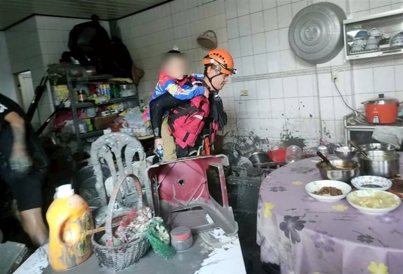 子供を背負い、泥まみれの住宅から避難する救助作業員＝新北市消防局提供（画像の一部を加工しています）