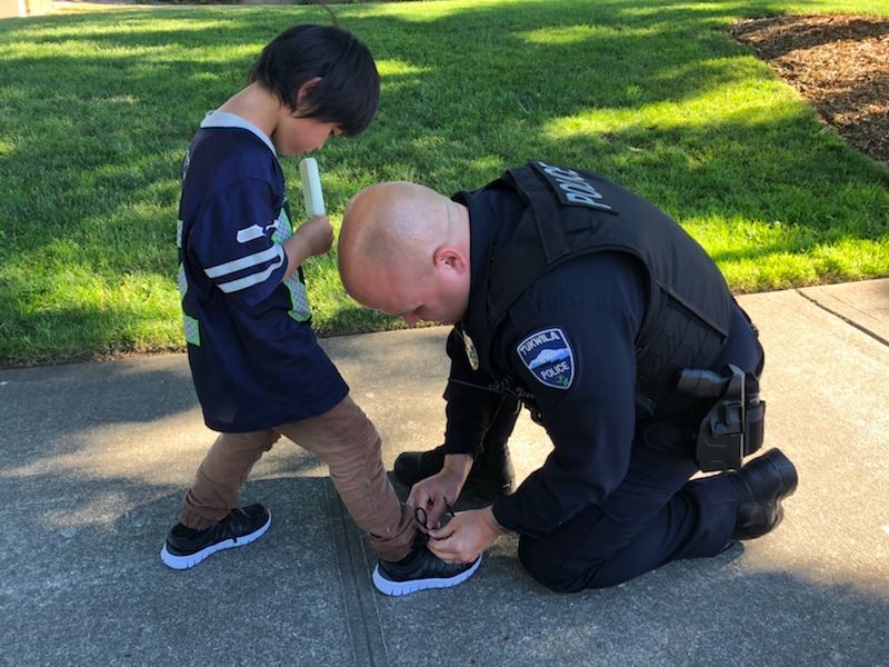 華盛頓塔克維拉警局公布一張照片,一名警察左腳跪地,彎下身來為一名穿著藍色球衫、棕色長褲的黑髮男童綁鞋帶,男童右手則拿著冰棒。(圖取自Tukwila Police Department臉書www.facebook.com/TukwilaPD/)