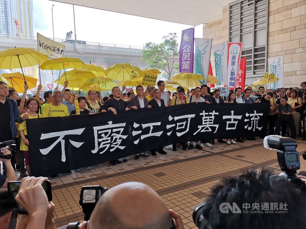 香港法院24日上午宣判占中案各名被告刑期前,9名被告包括「占中三子」在法庭前向媒體發表簡單談話,並與支持者撐黃傘,舉著「不廢江河萬古流」的標語。中央社記者張謙香港攝 108年4月24日