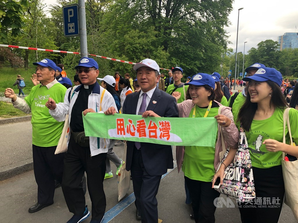 世界衛生組織(WHO)19日上午在聯合國歐洲總部前廣場舉辦Walk the Talk健走活動,世衛宣達團身穿TAIWAN CAN HELP的T恤上場。衛福部長陳時中(前排中)也手持「用心看台灣布條」參與。中央社記者戴雅真日內瓦攝 108年5月19日