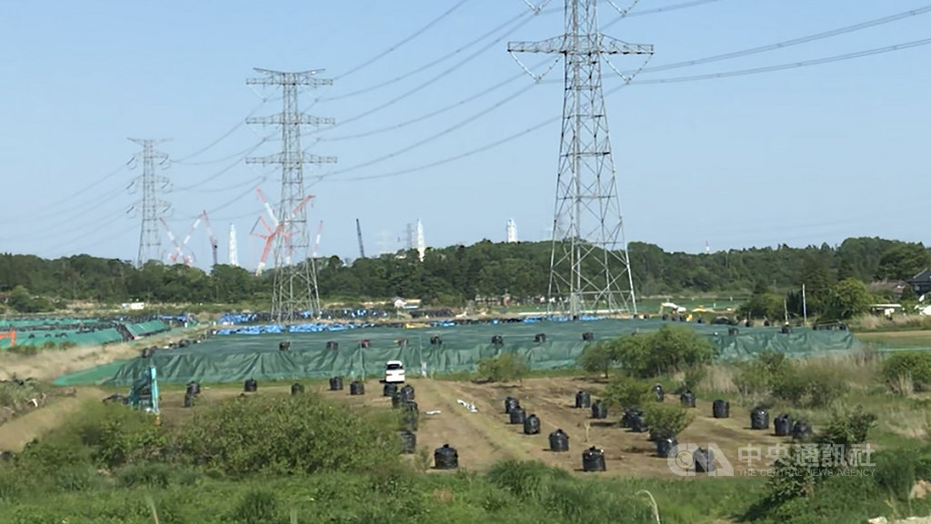 日本三一一震災後,福島第一核電廠周邊水土受到嚴重輻射污染,至今仍有部分區域為「核災返還困難區域」,沿途可見輻射量超標的廢土。圖後方白色柱狀物為福島第一核電廠煙囪。中央社記者梁珮綺福島攝 108年5月25日