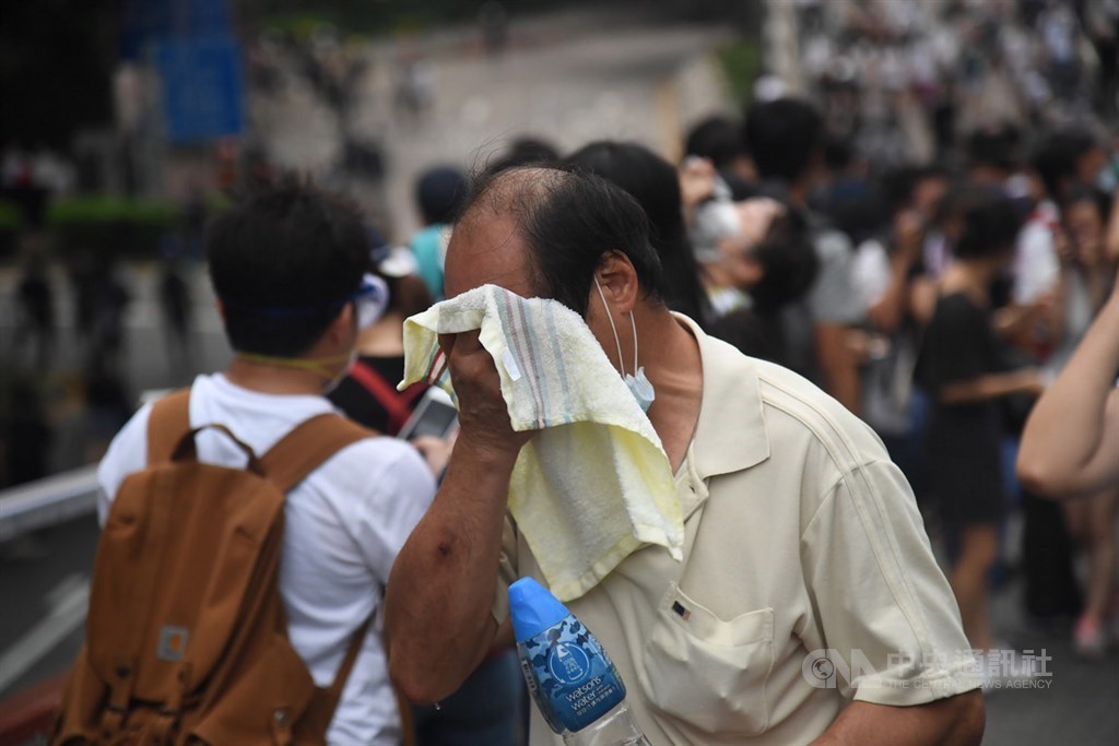 香港警方12日下午對集結抗議反送中的民眾施放催淚彈,強力驅散,外圍有民眾經不住刺激,以濕毛巾擦臉。中央社記者王飛華攝 108年6月12日