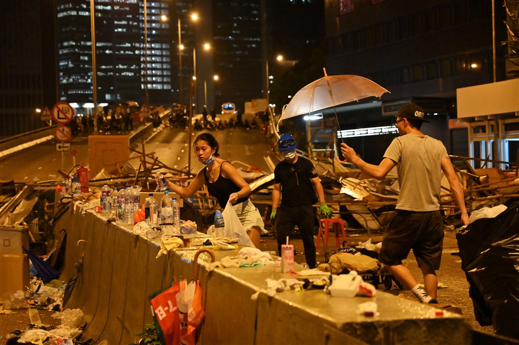 反對逃犯條例修正草案二讀的上萬名香港示威民眾至13日凌晨1時逐漸散去後,現場出現數名年輕人在路障後方撿拾垃圾。(法新社提供)