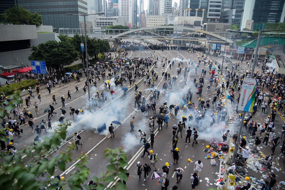 香港警察12日對「反送中」抗議展開清場,動用催淚彈,導致許多抗議民眾奔逃,但也有人上前用雨傘防止濃煙擴散,再使用礦泉水試圖稀釋煙霧。中央社記者侯文婷攝 108年6月12日