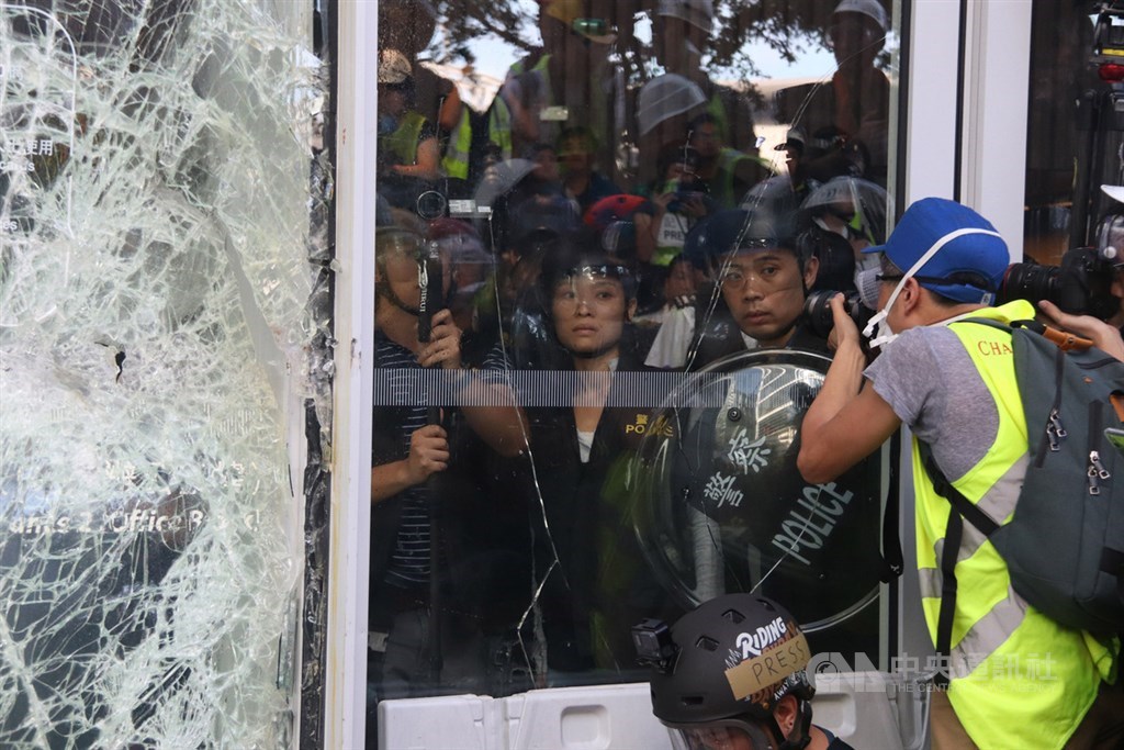 香港大批反修訂逃犯條例示威者1日衝撞立法會大樓,防暴警察在議會內戒備,但保持克制,並未衝出驅散群眾。圖為防暴警察看著外頭示威者,媒體記者趨前留下影像紀錄。中央社記者張謙香港攝 108年7月1日