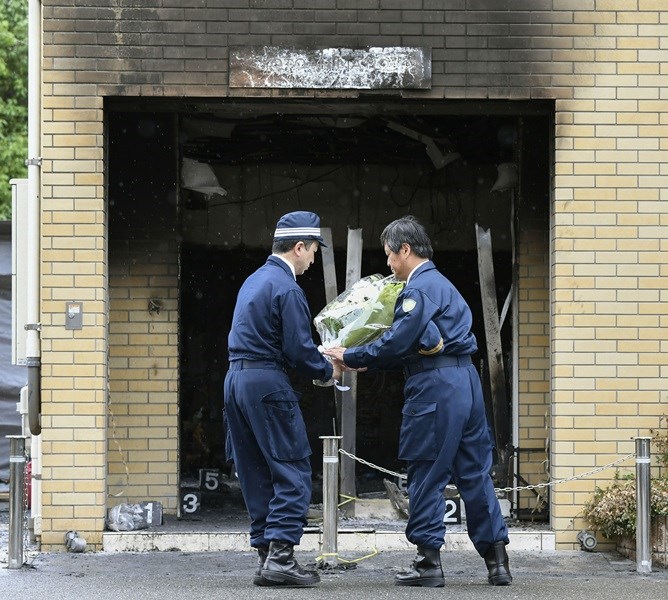 現場員警協助將民眾祈福花束放在京都動畫公司門口。(共同社提供)