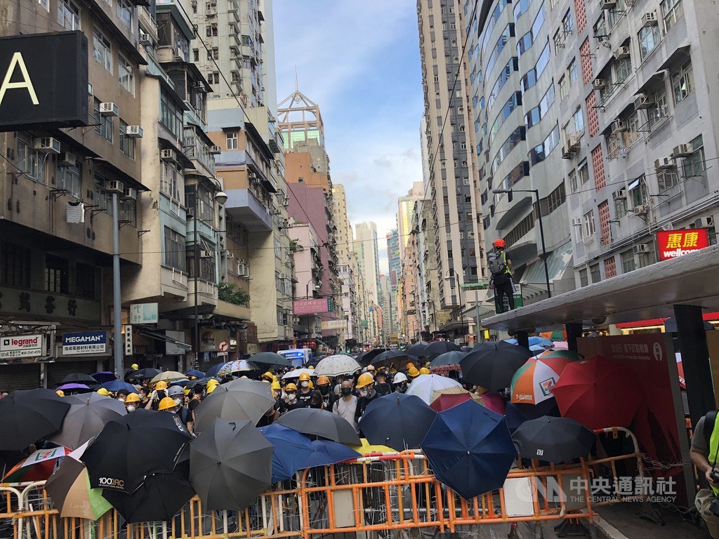 香港反送中自主遊行人士28日下午包圍中聯辦,港警晚間7時高舉黑旗,隨即施放催淚彈進行清場。圖為示威者下午在中聯辦大樓後方道路築起人牆防線。中央社記者廖漢原香港攝 108年7月28日