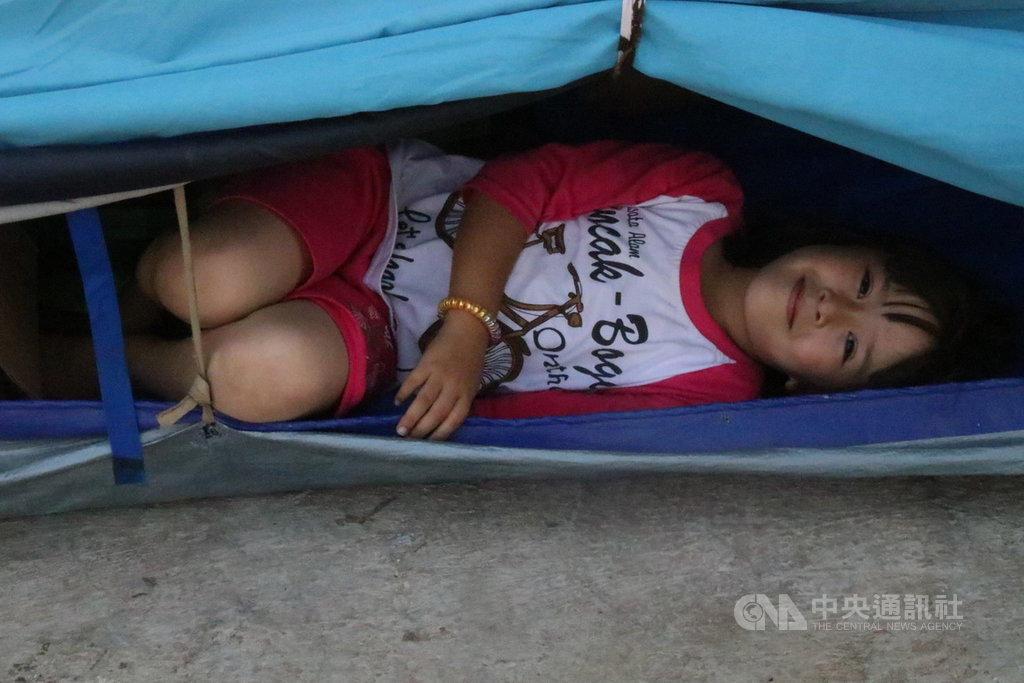 住在雅加達西區卡里德勒斯廢棄軍營難民營的阿富汗小女孩看到中央社記者前來採訪,好奇地從帳篷探頭出來看看,大方對攝影機微笑。中央社記者石秀娟雅加達攝。 108年8月3日