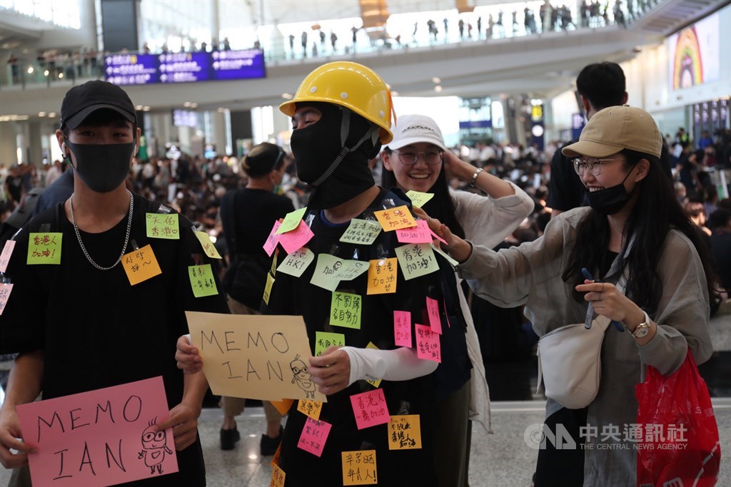 香港國際機場9日有「反送中」集會,下午2時左右,有數百人參加,他們穿著黑衣,坐在入境大廳上;青年讓民眾貼支持話語在身上。中央社記者吳家昇攝 108年8月9日